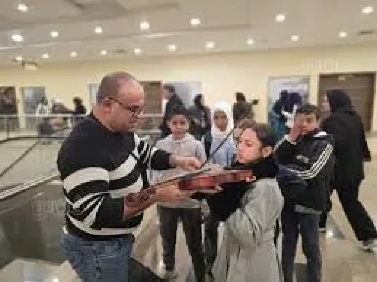 شاب يعلم اطفال بمعرض الكتاب فنون العزف